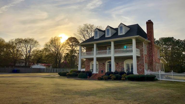 Brick Southern colonial home with white columns and a double front porch at golden hour, the kind of historic house found around Columbia, Tennessee