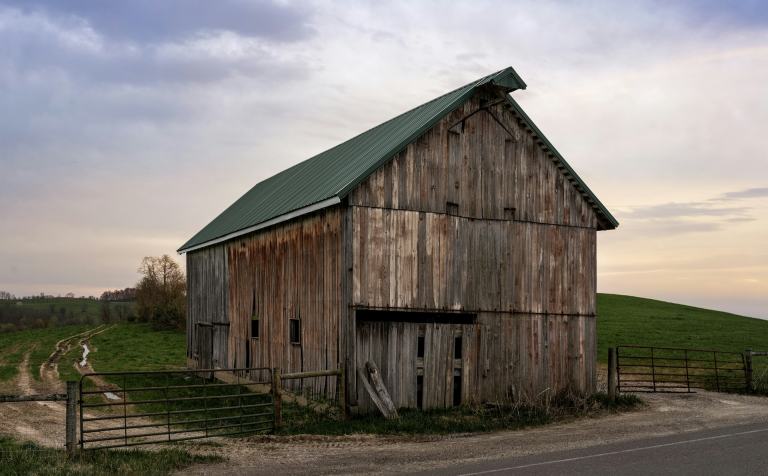 Weathered wood barn with a green metal roof beside a two-lane country road at dusk, the kind of rural scenery found around Leiper’s Fork, Tennessee