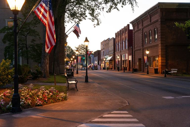 Small-town Tennessee main street at dusk with glowing lampposts, red brick storefronts and American flags