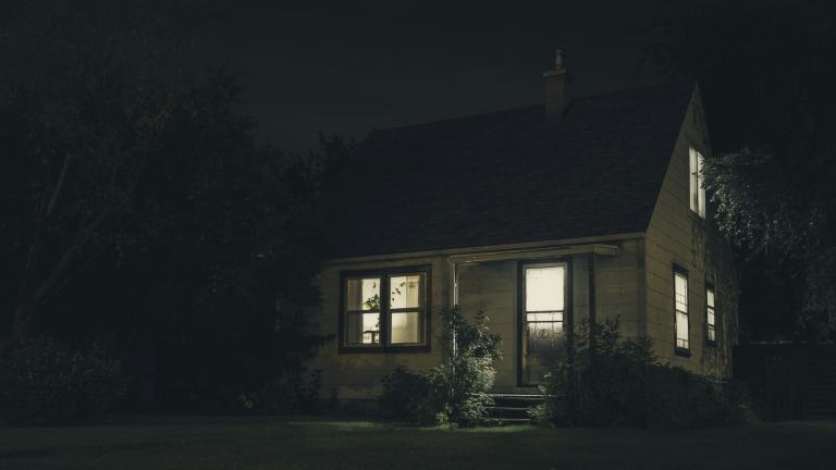 A small house at night with warm light glowing from its windows, the kind of evening when the lights, heat and air are all running